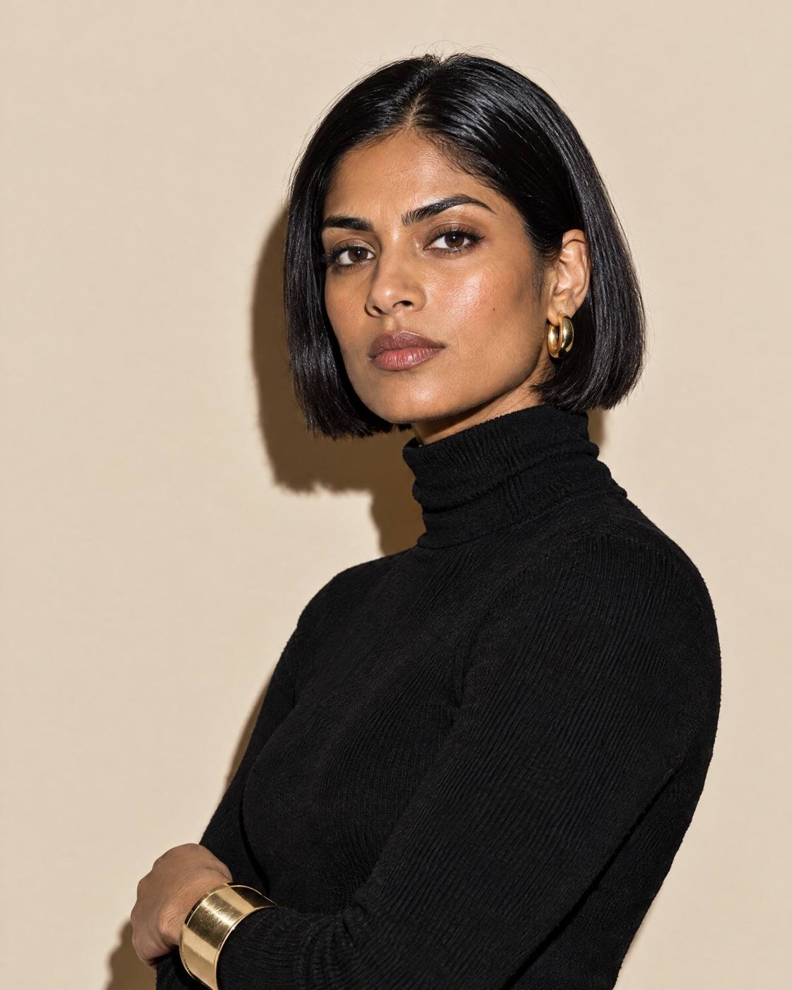 Studio portrait of a woman with a sleek chin-length bob in a black turtleneck, on bone paper.