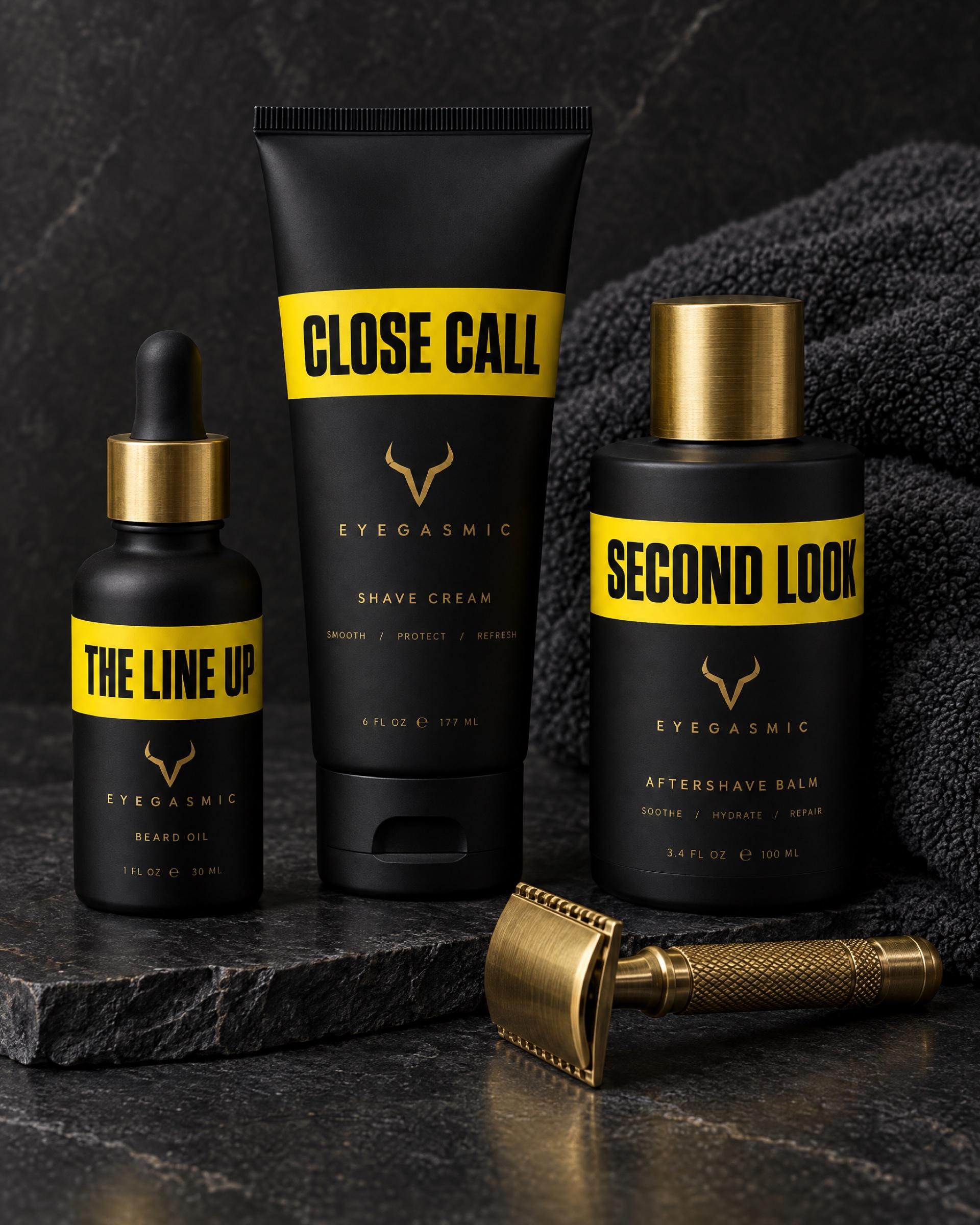 EYEGASMIC grooming in chrome yellow: The Line Up beard oil, Close Call shave cream and Second Look aftershave balm beside a brass safety razor and a charcoal towel.