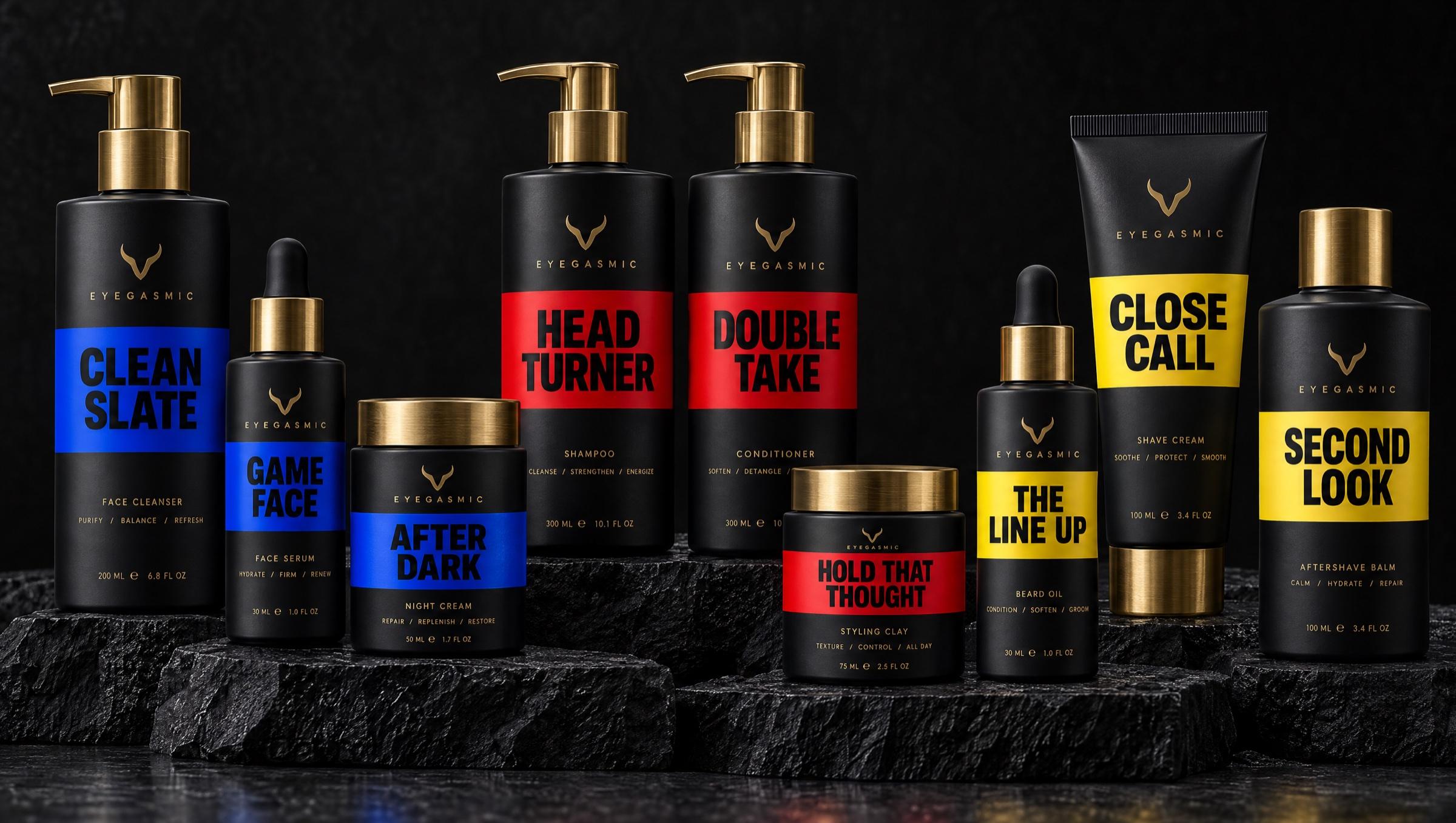 The full EYEGASMIC range on black stone: nine matte black products with brass caps and bold color bands, cobalt for skincare (Clean Slate, Game Face, After Dark), red for hair care (Head Turner, Double Take, Hold That Thought) and yellow for grooming (The Line Up, Close Call, Second Look).
