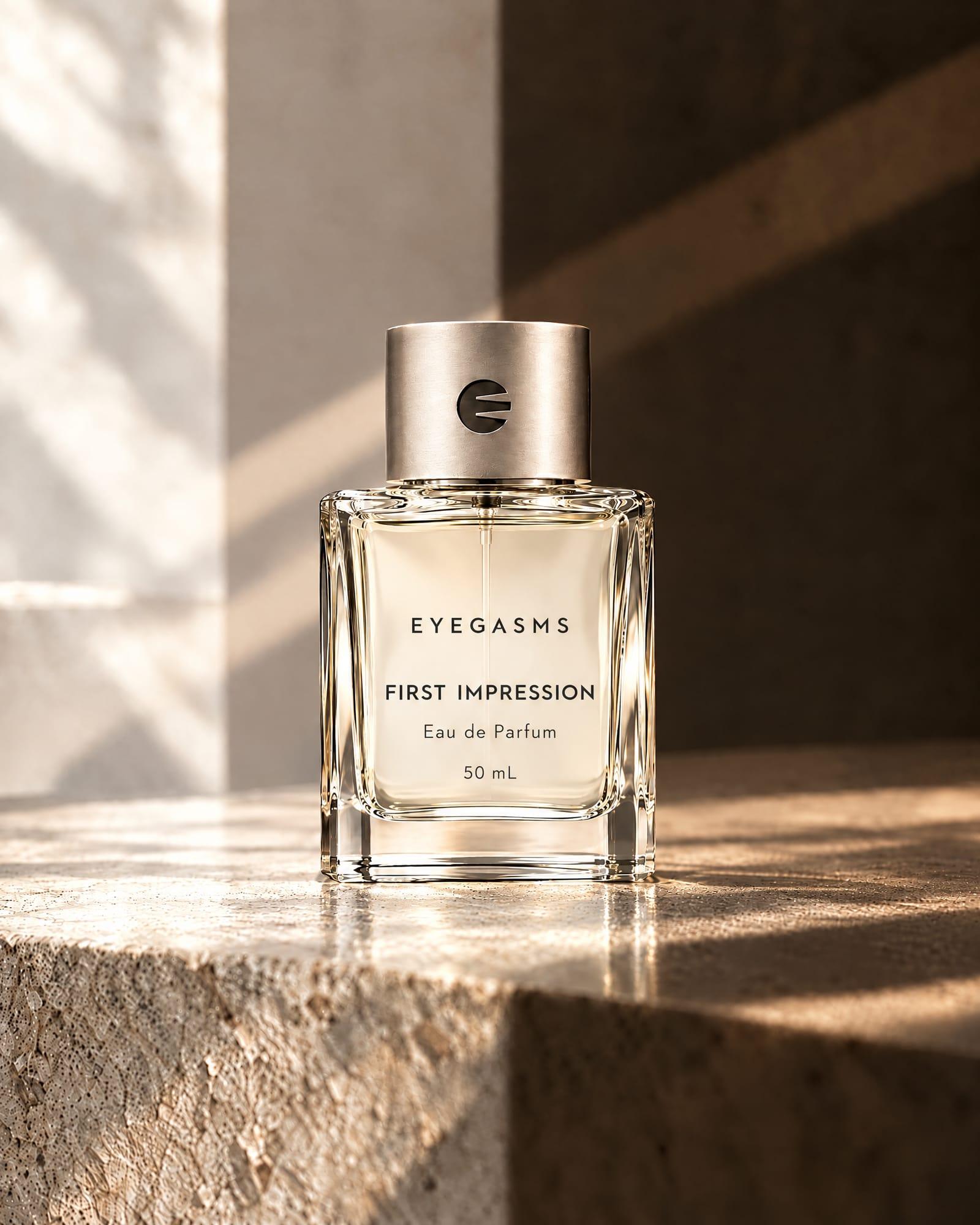 First Impression, eau de parfum, by EYEGASMS: a clear square glass flacon with a brushed silver cap, 50 mL, alone on a travertine ledge in raking golden light.