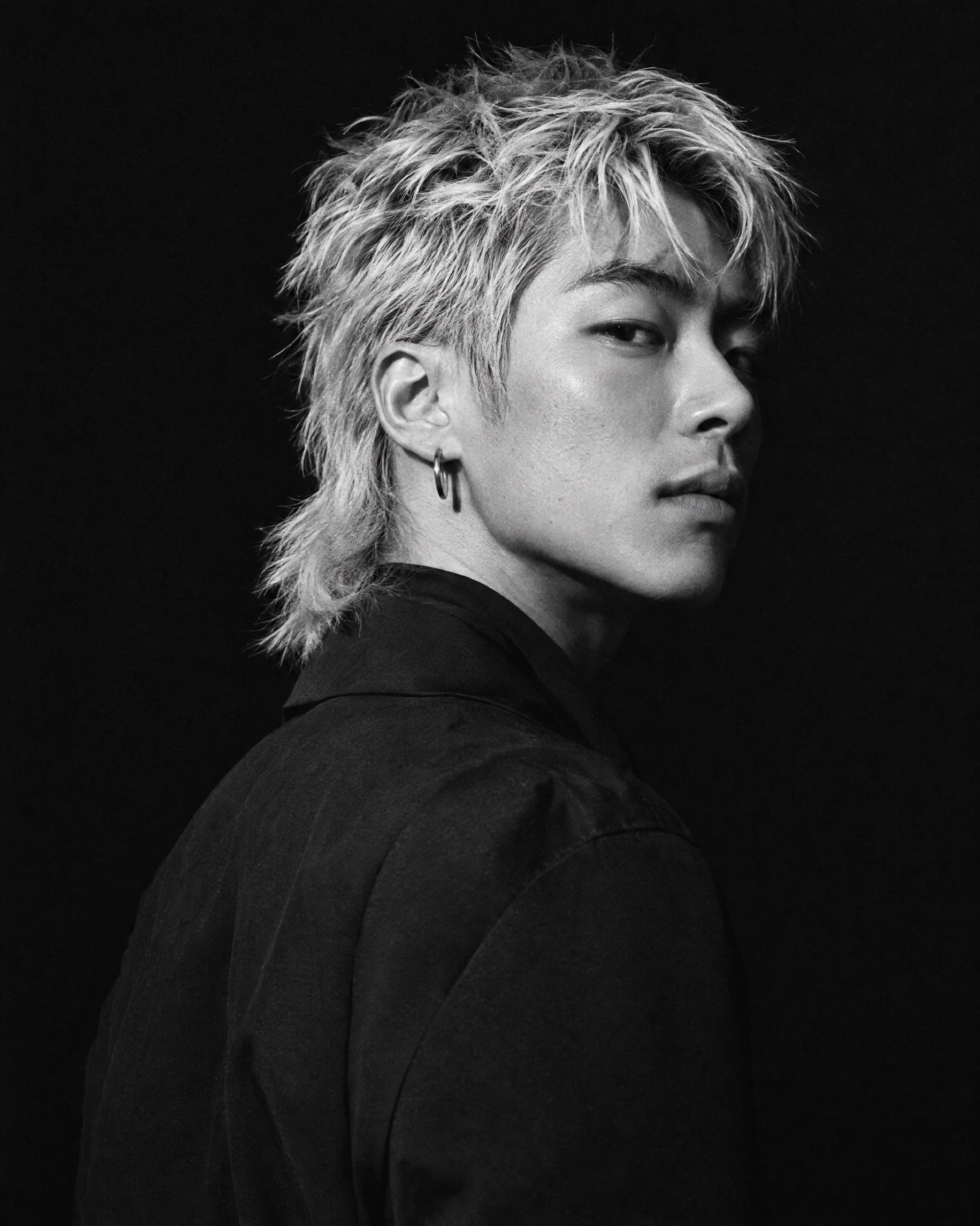 Black-and-white portrait of a young man with a platinum mullet looking over his shoulder.