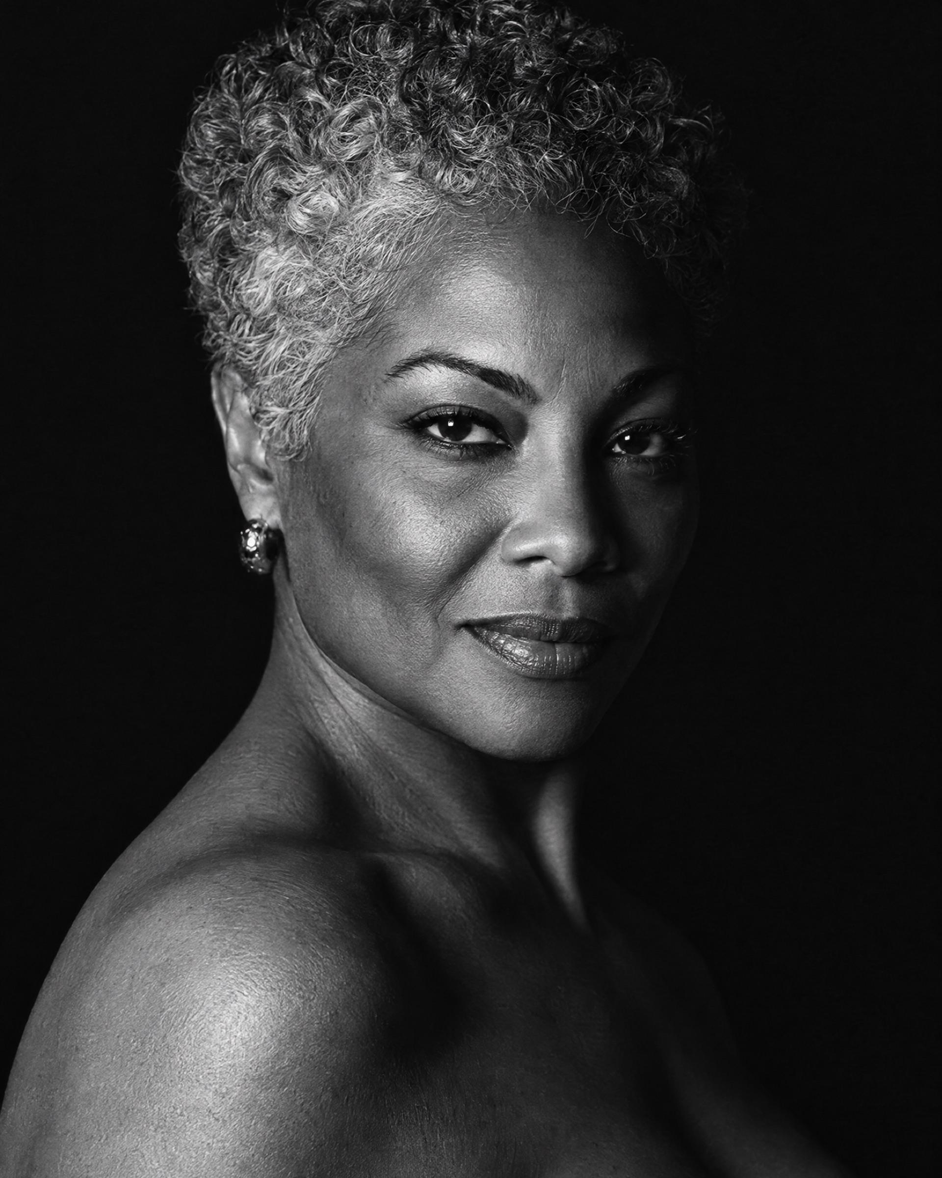 Black-and-white portrait of a woman with short silver curls and a knowing half-smile.