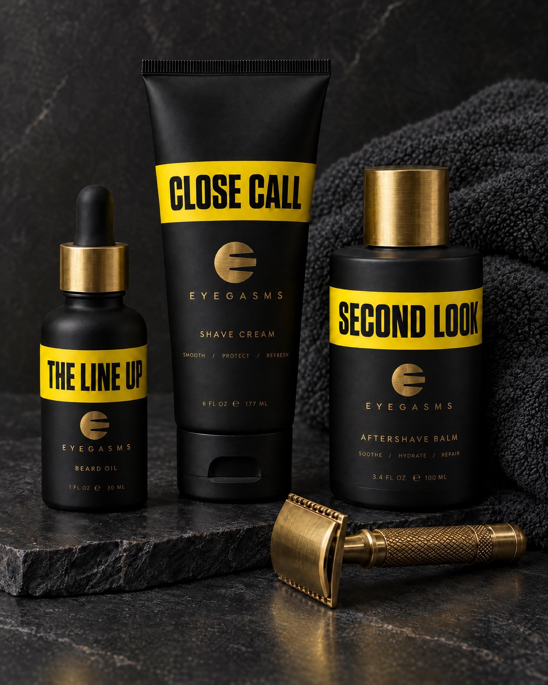 Grooming EYEGASMS en amarillo: aceite para barba The Line Up, crema de afeitar Close Call y bálsamo Second Look junto a una rasuradora de latón y una toalla gris oscuro.